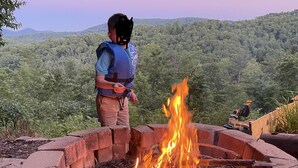A person standing by a fire pit in a natural setting with a forested hill in the background. - July4-7OPEN50%OFF❤️BESTMountainView/Hot Tub/ Pool Table  /Ping Pong Table/ Wifi  (Blue Ridge)