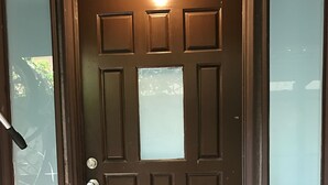 A brown door with a keyhole and a doorknob, flanked by frosted glass panels.