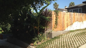 A residential backyard with a wooden fence, a concrete planter, and a lawn with a patterned walkway.