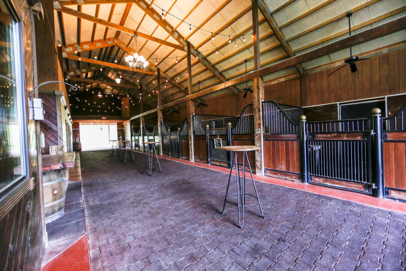 An indoor stable with wooden stalls, a brick floor, and a high ceiling with exposed beams.