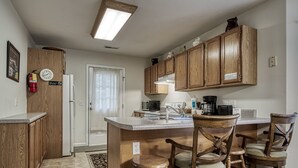 A kitchen with wooden cabinets, a central island with stools, a refrigerator, and a microwave.