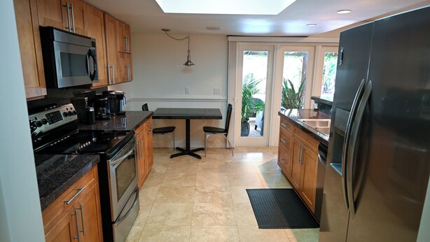 A modern kitchen with wooden cabinets, stainless steel appliances, and a dining area with a table and chairs. - Modern Tropical Pool Home ⭐️ (Orlando)