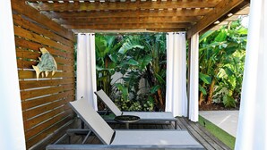 A wooden deck with two lounge chairs and a small table, surrounded by lush tropical plants. - Modern Tropical Pool Home ⭐️ (Orlando)