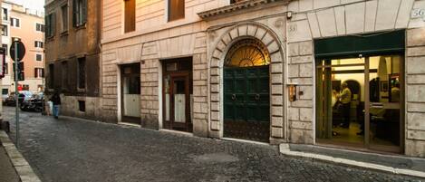 A historic building with a cobblestone street, a green door, and a shop with large windows.