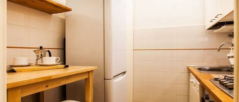 A compact kitchen with a white refrigerator, wooden countertop, two stools, and a stove.