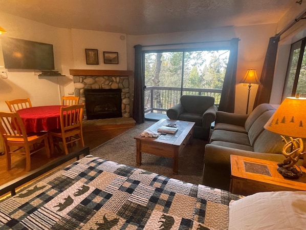 A cozy living room with a fireplace, a dining area with a red tablecloth, and a comfortable sofa.