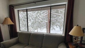 Un salon avec un canapé, deux lampes et une fenêtre donnant sur des arbres couverts de neige.