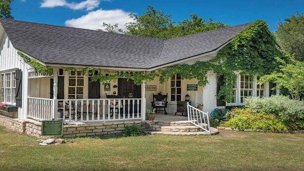 A white building with a porch, stone steps, and a sign indicating 'The Pristine Room'. - Prairie House. River Cabin. Sleeps 8 (Glen Rose)