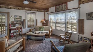 A cozy living room with a sofa, chairs, a coffee table, and a fireplace. There are wooden shutters on the windows, and a sign that reads "CANDLES" above the fireplace. - Prairie House. River Cabin. Sleeps 8 (Glen Rose)