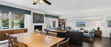 A spacious living room with a fireplace, dining area, and a large window overlooking a garden.