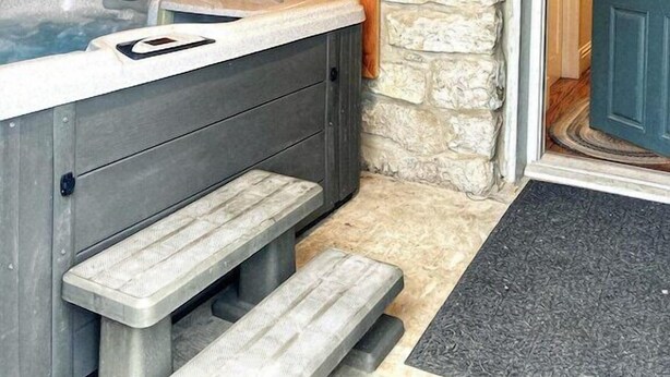 A spa area with a hot tub, wooden cabinets, stone walls, and a door. - 1870's Luxury Guest Cottage, Historic Downtown St. Charles, Mo. (St. Charles)