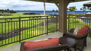 Un balcone con mobili in vimini che si affaccia su un campo da golf e vista sull'oceano.