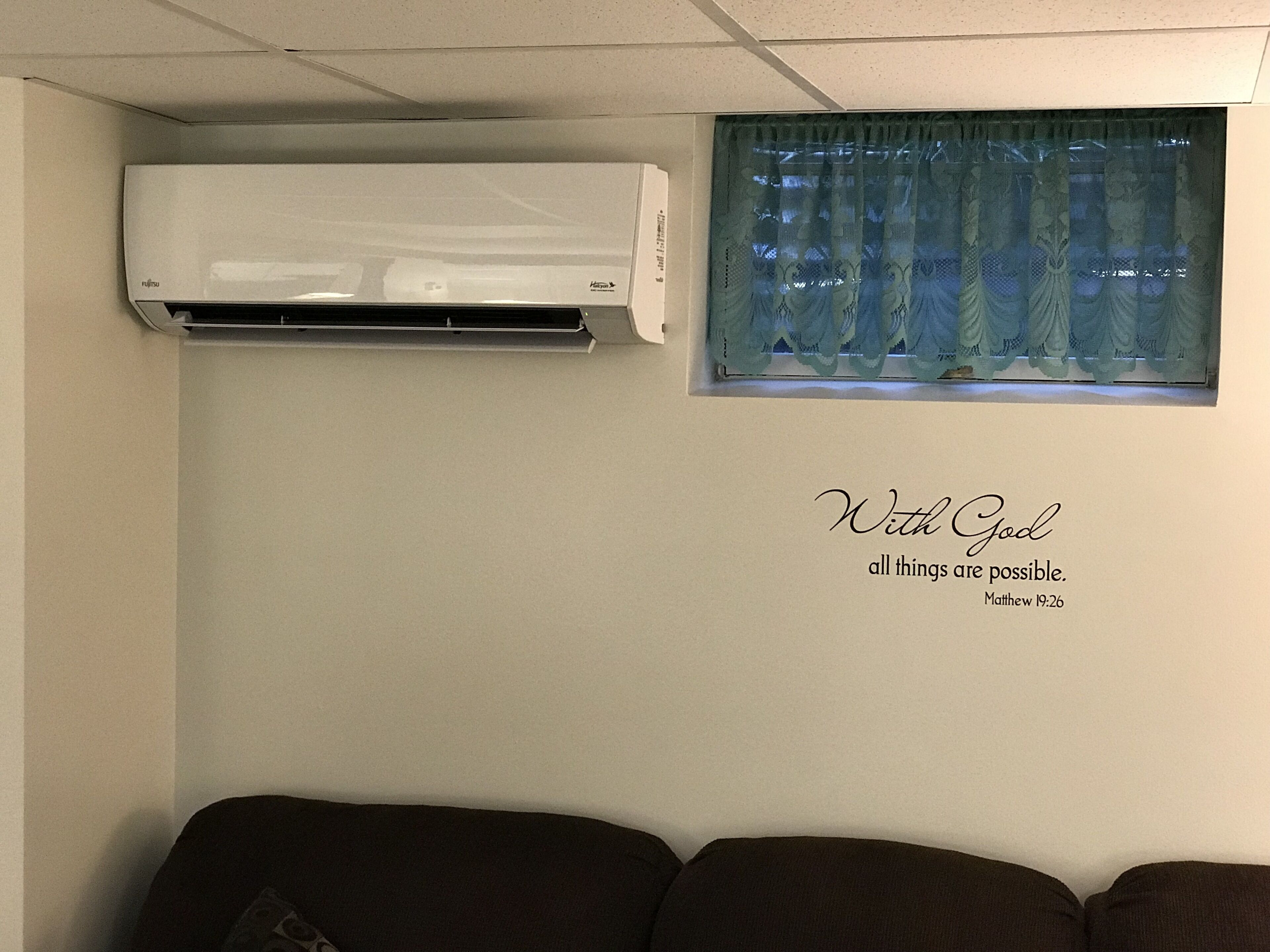 A room with a wall-mounted air conditioner, a window with lace curtains, and a motivational quote.
