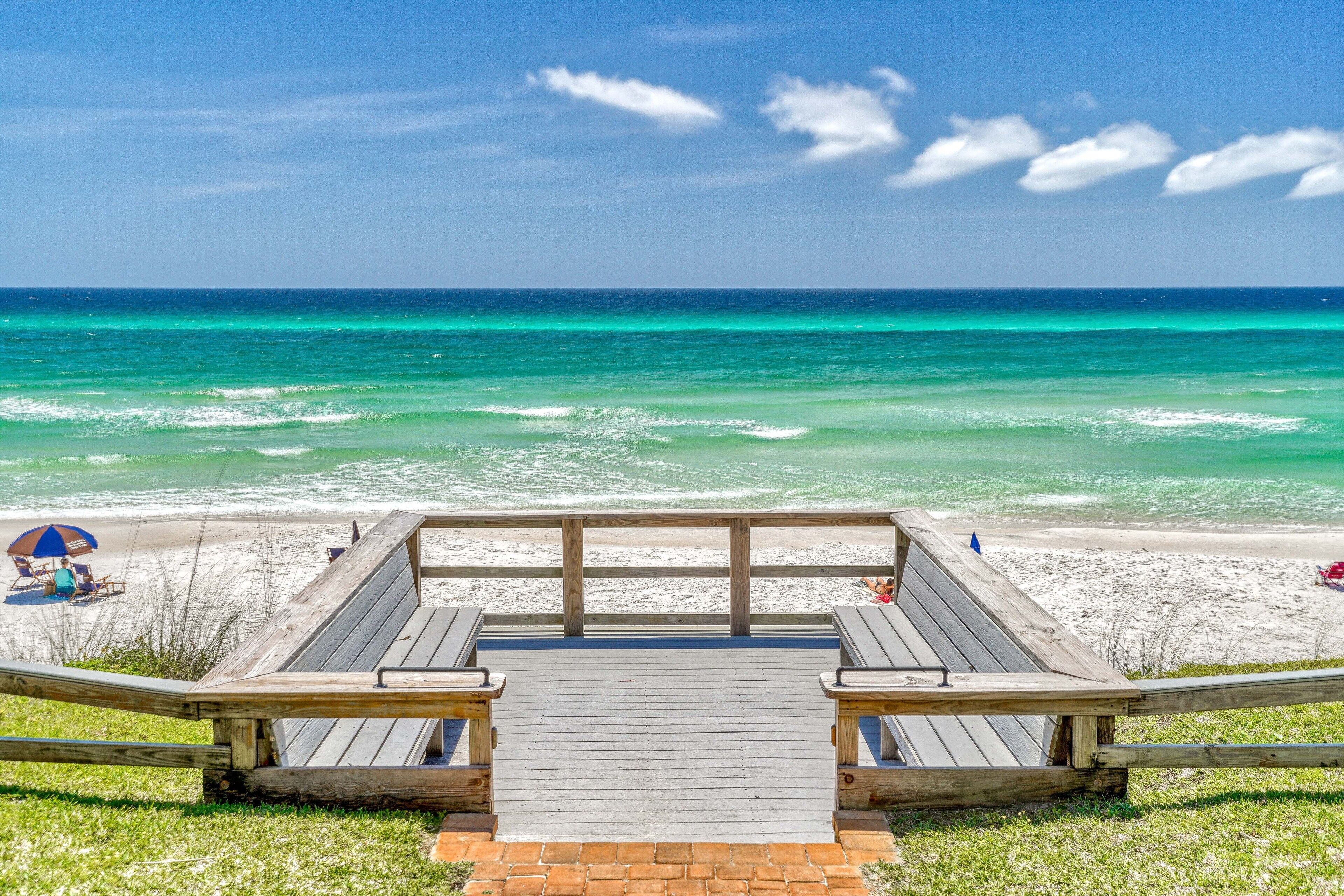 Un paseo marítimo de madera que conduce a una playa con vista despejada al océano.