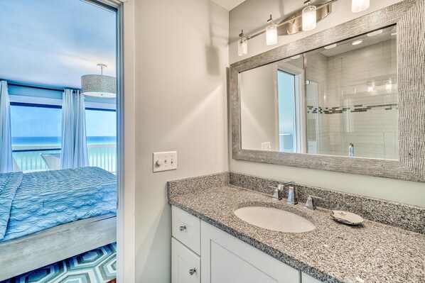 A modern bathroom with a granite countertop, a large mirror, and a view of the ocean through a window.