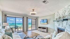 A living room with a view of the ocean, a stone fireplace, and a television on the wall.
