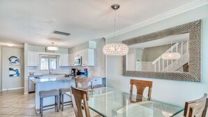 A modern kitchen with white cabinets, a central island, and a dining area with a glass table and wooden chairs.