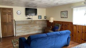 Un salon avec un canapé bleu, une cheminée, un téléviseur et une porte en bois.