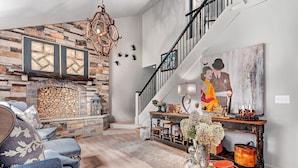 Un salon avec une cheminée en pierre, un escalier et un tableau accroché au mur.