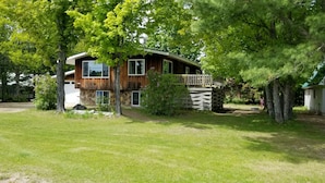 Een houten chalet met twee verdiepingen en een stenen fundering, omgeven door weelderige begroeiing en bomen.