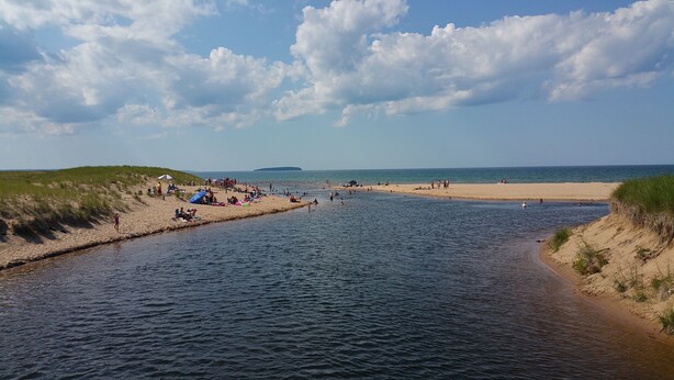 Een strand met mensen die zonnebaden en zwemmen, een zandstrand en een rustige zee.