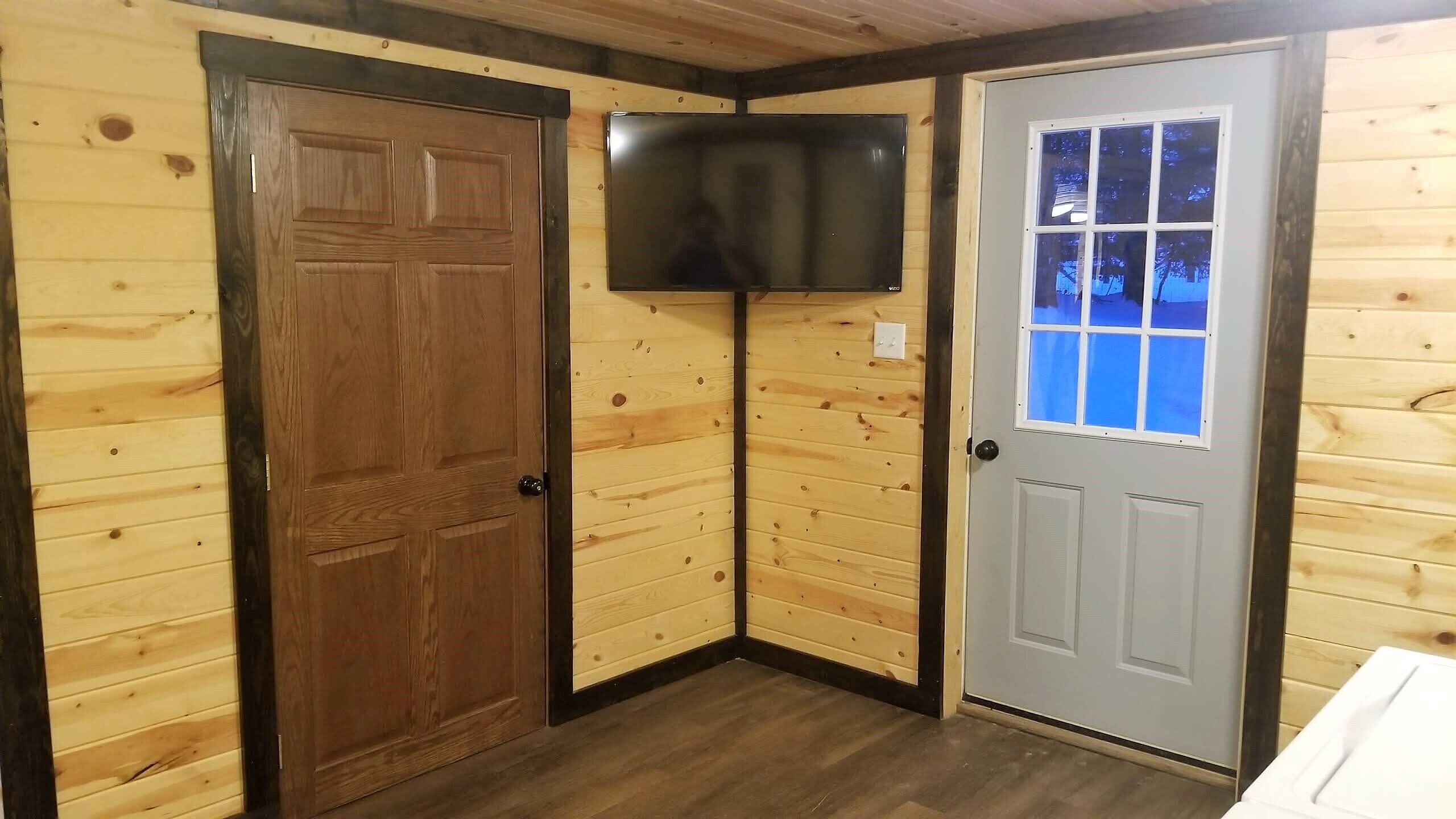Une pièce d’angle avec des murs en bois, une porte, une fenêtre et un téléviseur fixé au mur.