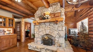 A rustic cabin interior with a stone fireplace, wooden beams, and a wooden bar area.