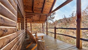 A wooden deck with a rustic log cabin structure, a wooden chair, and a small wooden stool.