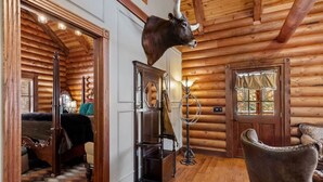 A log cabin interior with a bed, a chair, a lamp, and a mounted bull head.