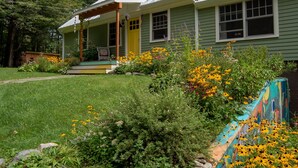 A green house with a porch, surrounded by a garden with various plants and flowers.