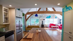 A spacious kitchen with wooden beams, a dining area with a long table, and a living room with a red sofa and a fireplace.