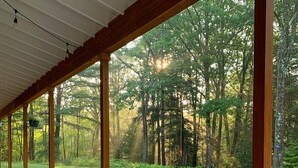 A covered outdoor deck with a wooden table and a mug, overlooking a forested area.