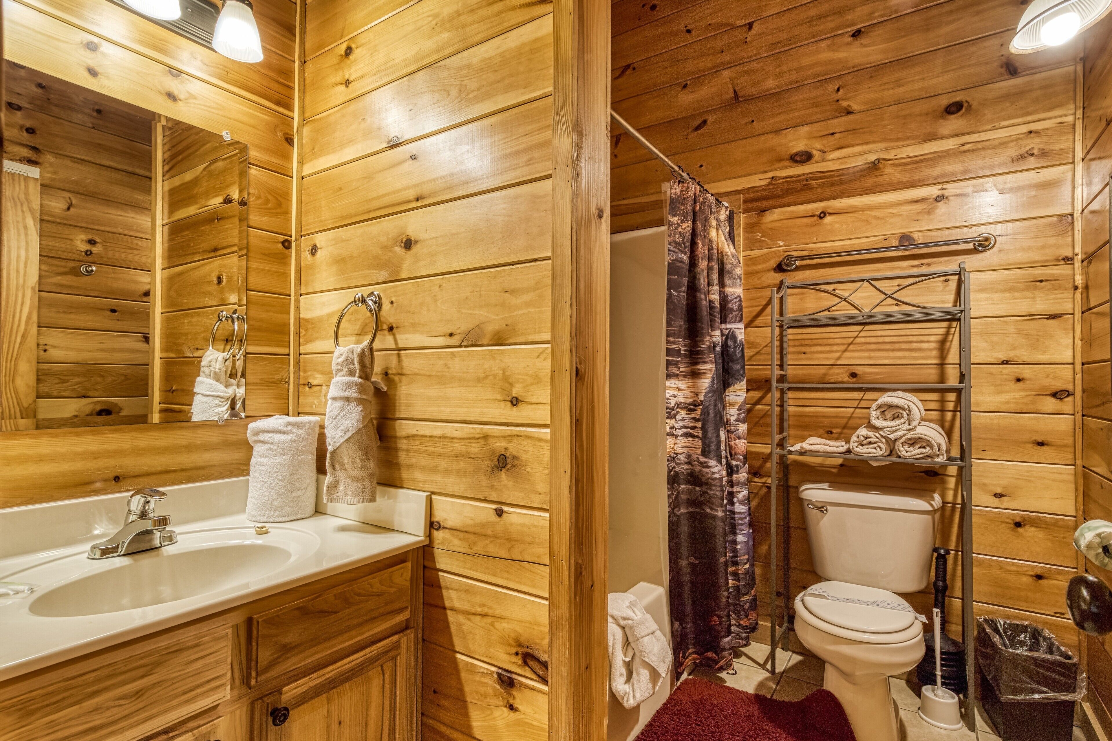 Une salle de bain rustique, aménagée dans une cabane en bois, avec un lavabo, un miroir, des toilettes et un rideau de douche.