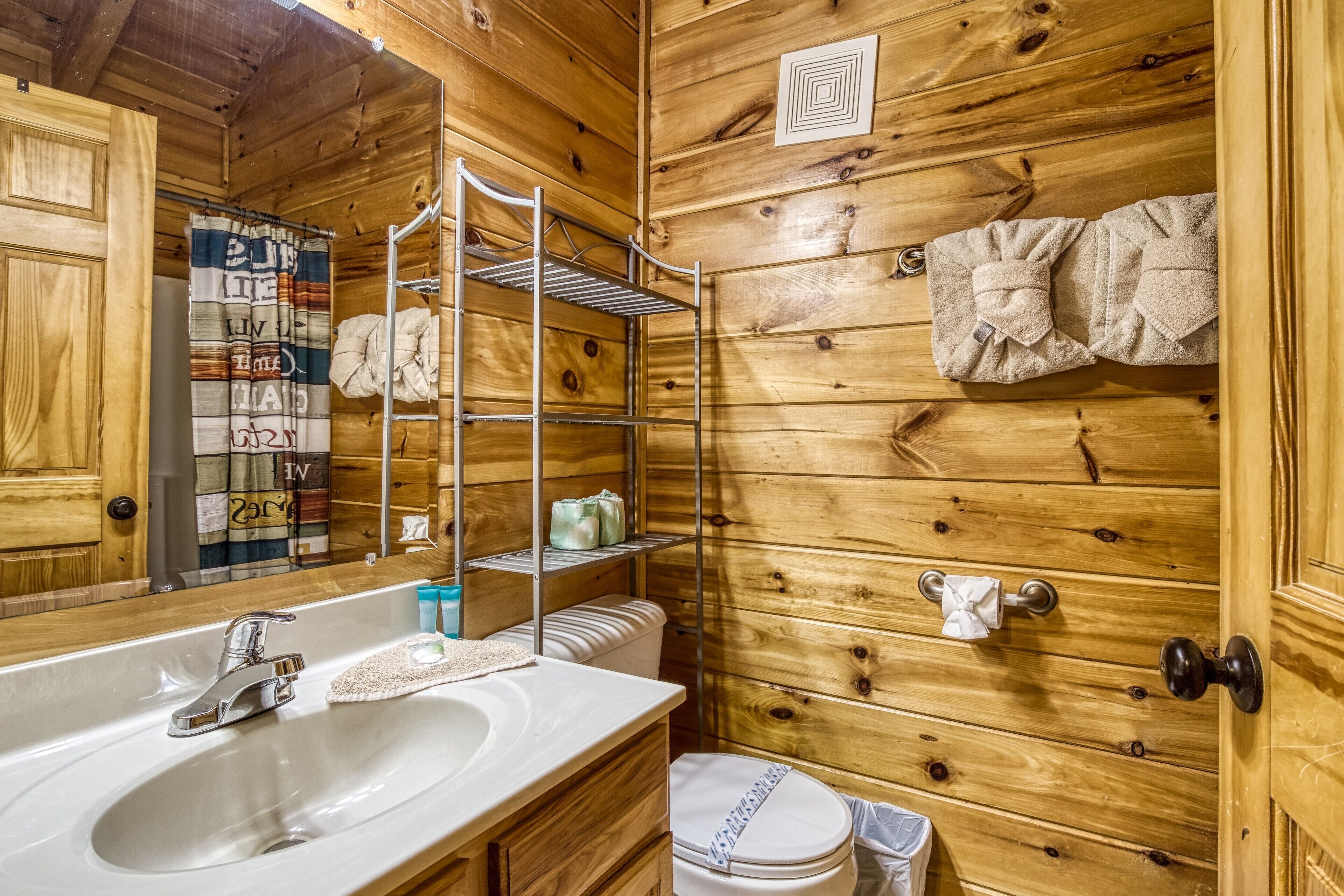 Een houten badkamer in een blokhut met een wastafel, toilet en handdoekhouder.