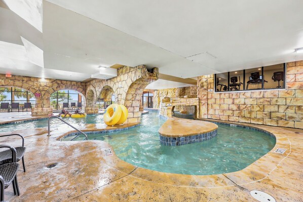 An indoor swimming pool with a stone wall, a hot tub, and exercise equipment.