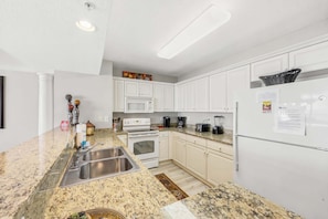 Una cocina con gabinetes blancos, encimera de granito, microondas, estufa, pileta y refrigerador.