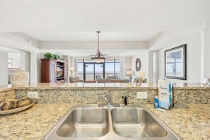 Una cocina con encimeras de granito, fregaderos de acero inoxidable y vistas al área de estar.