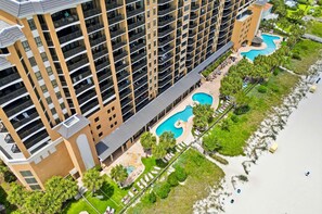 A high-rise hotel with multiple balconies, a swimming pool, and a beach area.