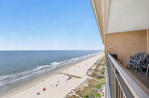 A balcony with a view of a beach, outdoor furniture, and a wooden deck.