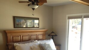 A bedroom with a wooden headboard, a ceiling fan, a bedside lamp, and a window with blinds. - Beautiful river home with large yard, sitting area and fire pit! (Estes Park)
