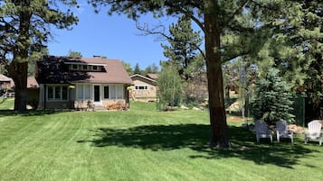 A two-story house with a well-maintained lawn, a patio with outdoor furniture, and a large tree in the foreground.