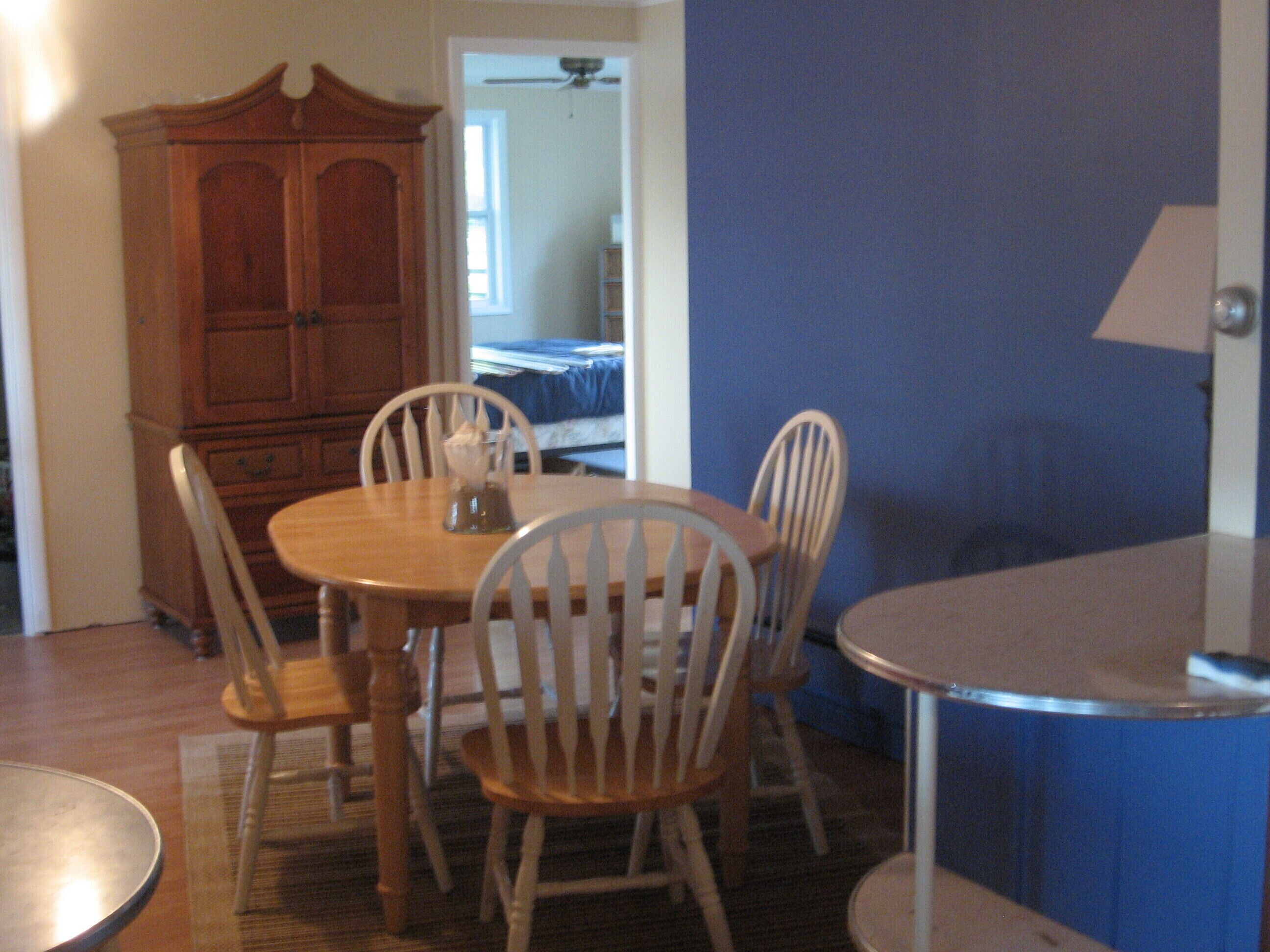 Un comedor con una mesa y sillas de madera, un armario y una cama al fondo.
