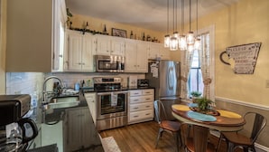 A kitchen with white cabinets, stainless steel appliances, a dining table with chairs, and a decorative sign on the wall. -  SPACIOUS HISTORIC DOWNTOWN LOFT!  BEST LOCATION IN THE HEART OF TOWN! (Hermann)