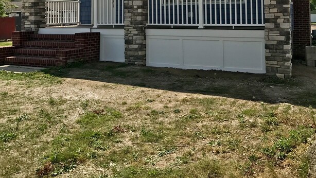 Una casa de dos pisos con porche delantero, pilares de piedra y garaje.
