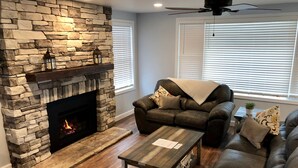 Una sala de estar con chimenea de piedra, sofás de cuero, una mesa de centro y un ventilador de techo.