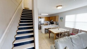 A kitchen with a central island, a dining area with a table and chairs, and a staircase leading to another level. -     Sun, Sand & Serenity — Your Gulf Getaway Awaits (Gulf Shores)