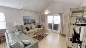 A living room with a sofa, a coffee table, a ceiling fan, and a sliding glass door leading to a balcony. -     Sun, Sand & Serenity — Your Gulf Getaway Awaits (Gulf Shores)