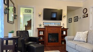 A living room with a fireplace, a television, a sofa, and a chair. - Cape May Jackson Street Beach Rental with Ocean Views (Cape May)