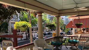 A covered outdoor seating area with wicker chairs and tables, a hanging flower planter, and a sign for 'The Puffin'. - Cape May Jackson Street Beach Rental with Ocean Views (Cape May)