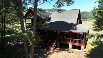 Escape to a serene retreat surrounded by lush greenery, featuring a spacious main cabin with a cozy porch and separate upper level.